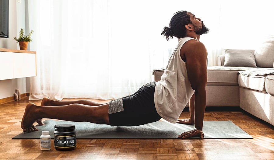Male doing yoga on the floor in living room with sports supplements 