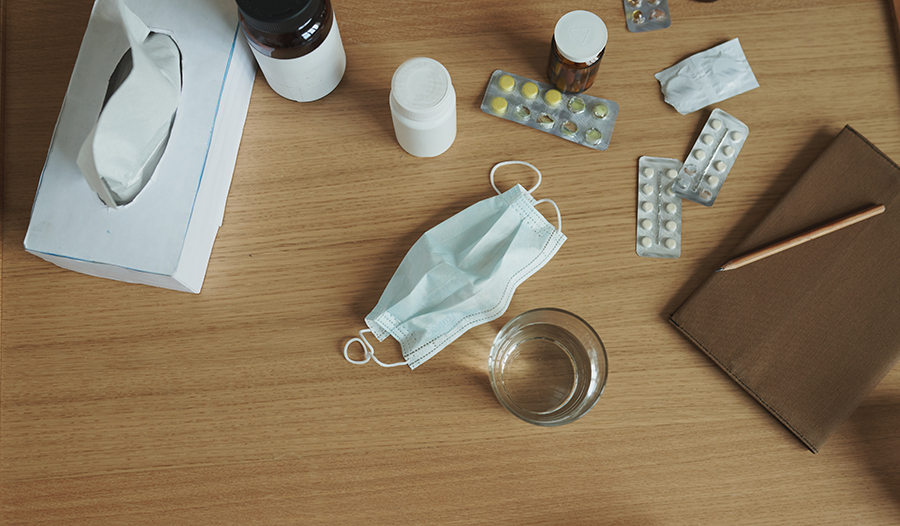 Flat lay of mask, tissues, vitamins, glass of water on wooden table