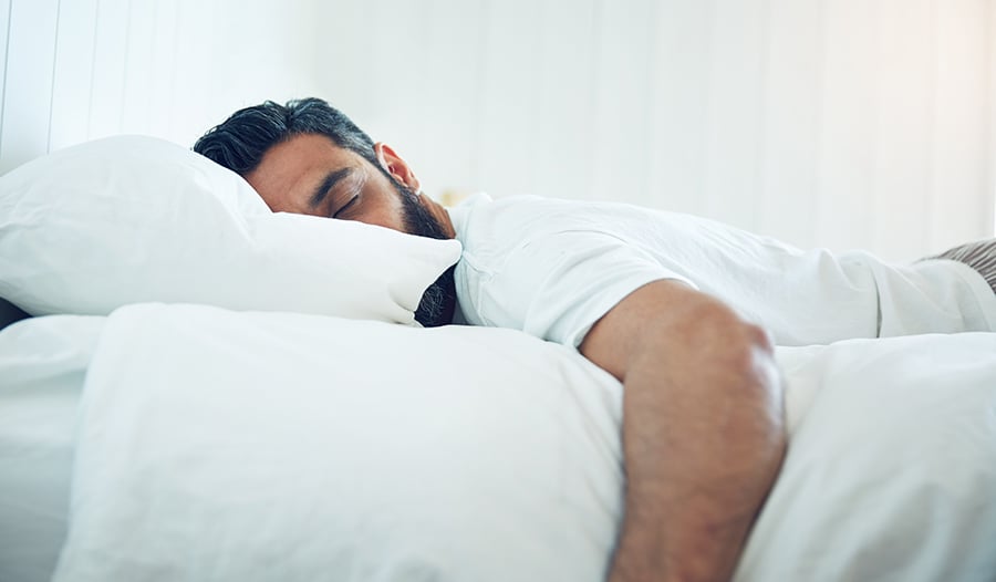 Brunette man with beard asleep in bed with white sheets 