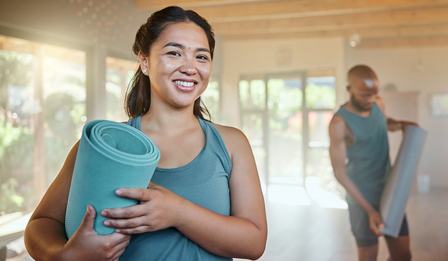 Healthy young woman smiling holding yoga mat after yoga class