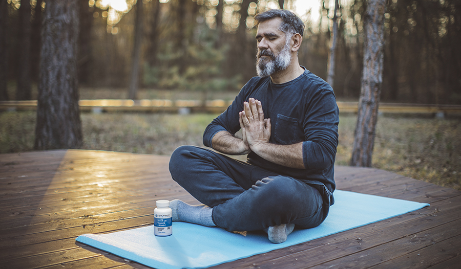 Older man meditating outside on a yoga mat with 5-HTP supplement