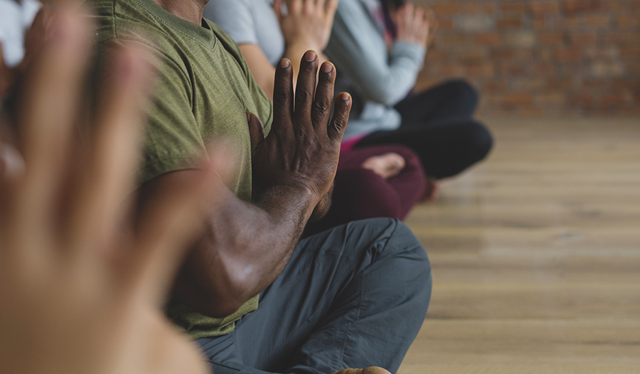 Man in green shirt in a group of people meditating with hands together in prayer