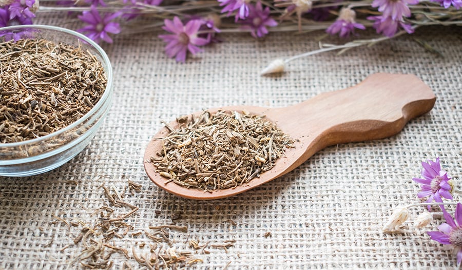 Valerian root in wooden spoon with purple flowers
