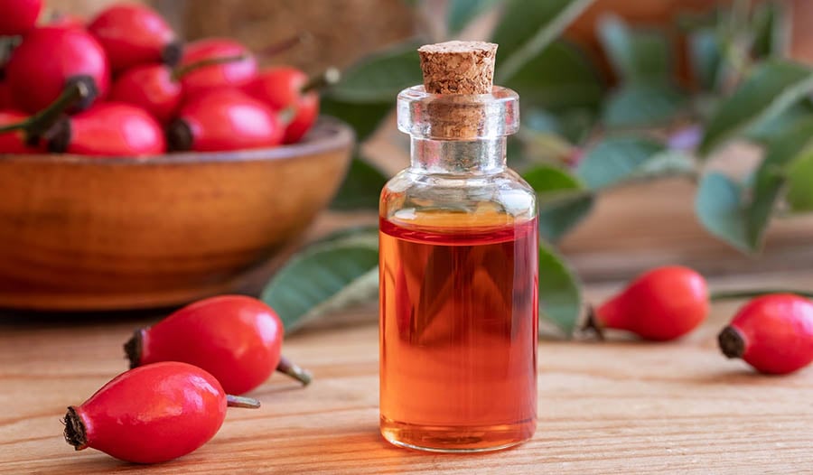 Rosehip oil in glass bottle on table with rosehip buds 