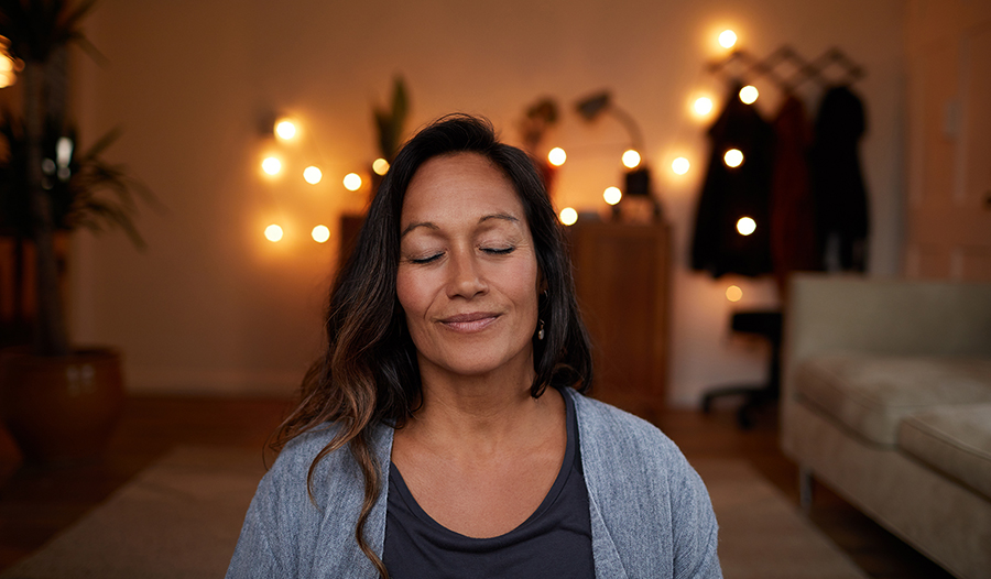 Meditating woman smiling with her eyes closed while sitting on her living room floor practicing yoga