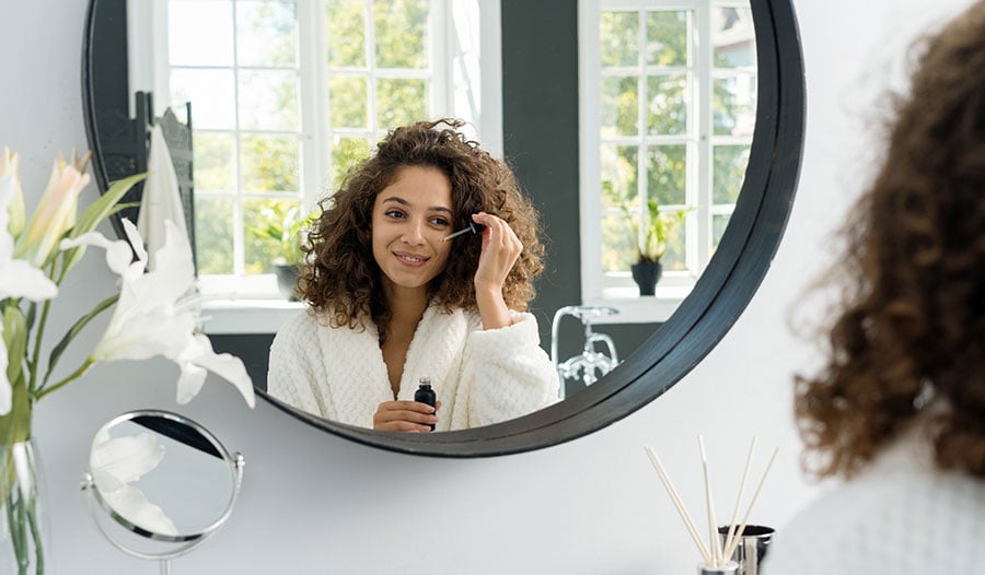 woman applying skincare serum with adaptogens in the mirror