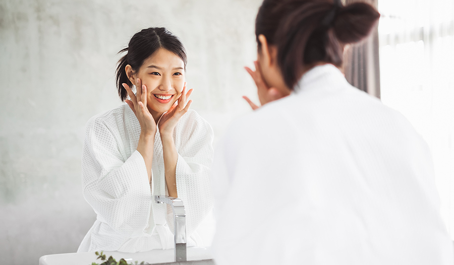 Asian woman washing face and applying skincare products in bathroom