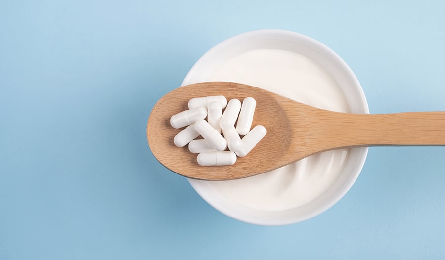 Probiotic supplement on wooden spoon over bowl of yogurt