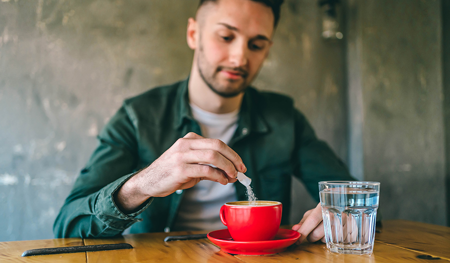 Man adding sugar to his coffee sitting at a table