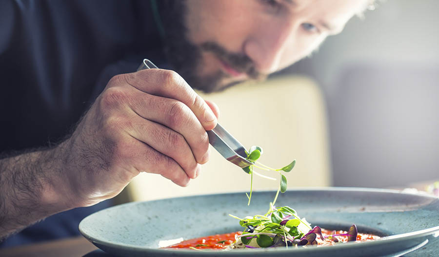 Chef preparing dish adding green garnish