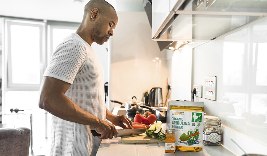 Man cooking healthy dinner in kitchen with vegetables, spirulina, and turmeric