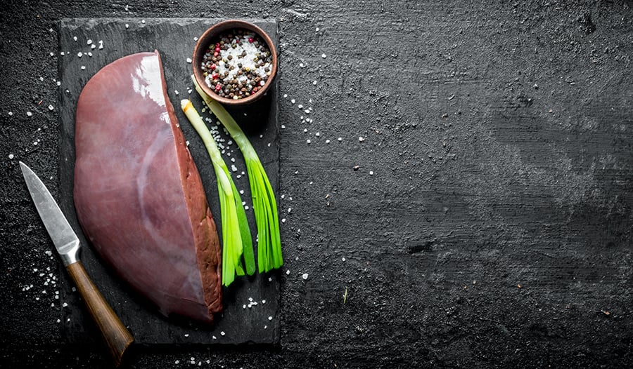 Beef liver with knife, salt, and green onion on cutting board