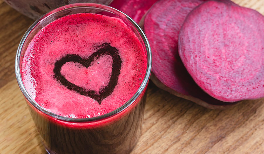 Beet juice with heart and raw beets on table