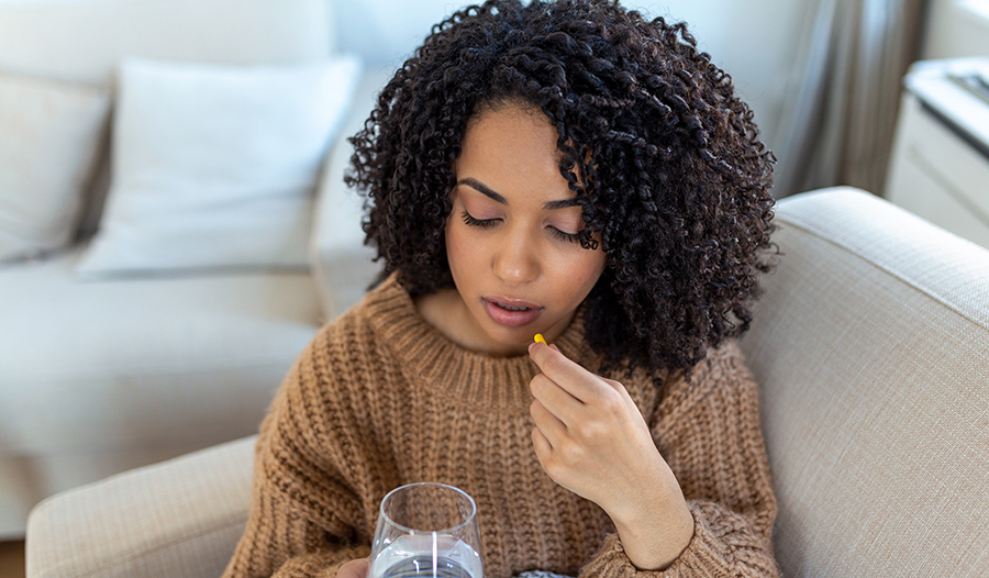 Young woman taking vitamin or supplement with water