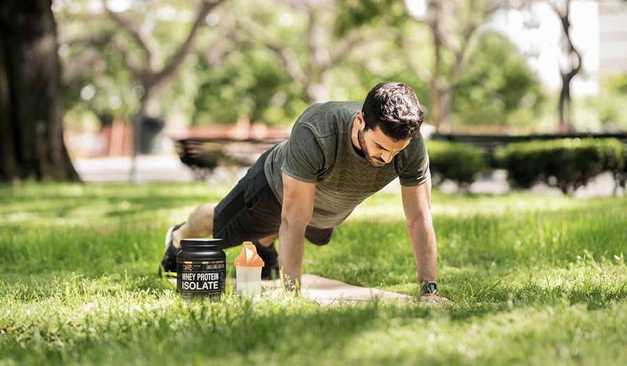 Man in park exercising holding a plank in the grass with protein shake