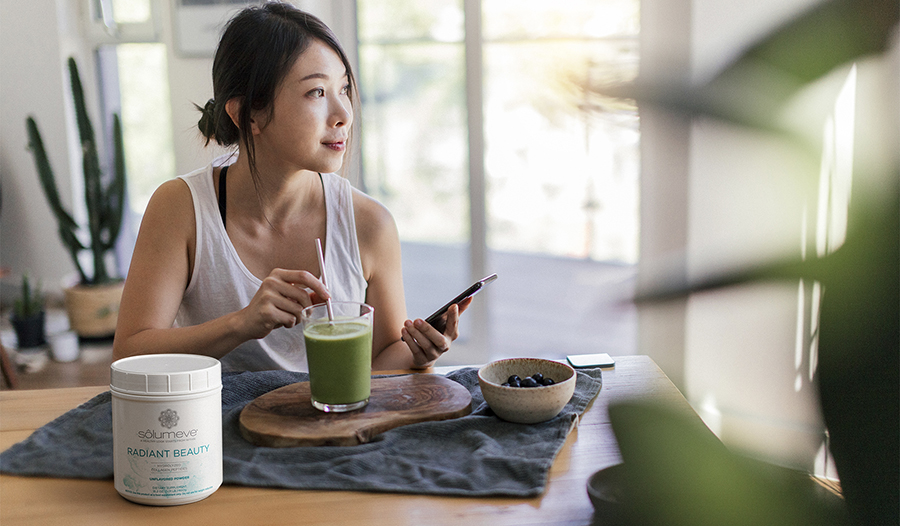 Healthy woman drinking collagen smoothie in her kitchen looking out window