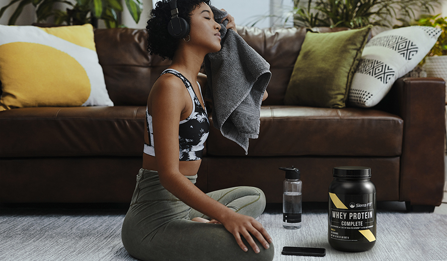 Woman sitting on floor wearing headphones wiping sweat after at home workout