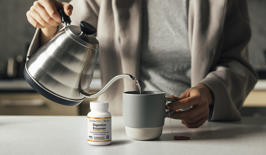 Woman pouring hot water into cup with tea bag and digestive enzymes on the table