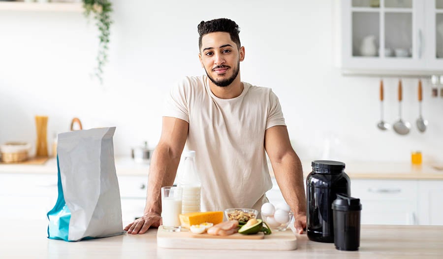 Fit male in kitchen with healthy food and protein supplements