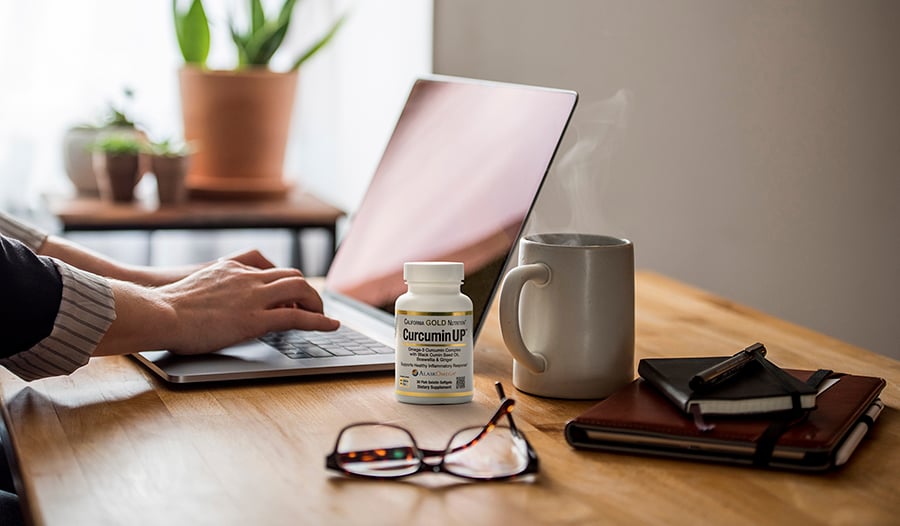 Turmeric supplement on desk with laptop, glasses, and coffee