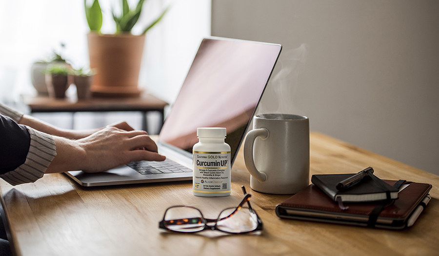 Turmeric supplement on desk with laptop, glasses, and coffee