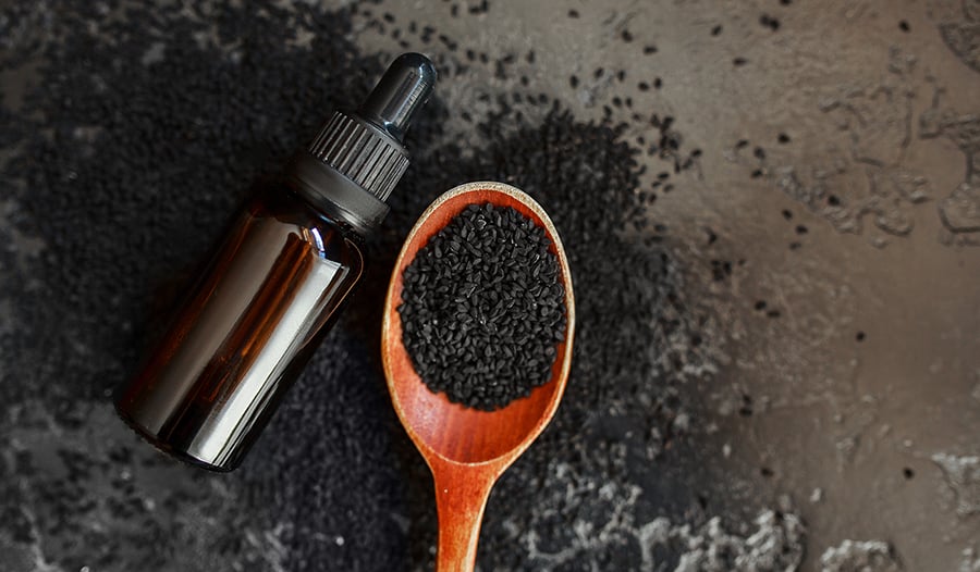 Black seed oil and black seeds with wooden spoon on stone table