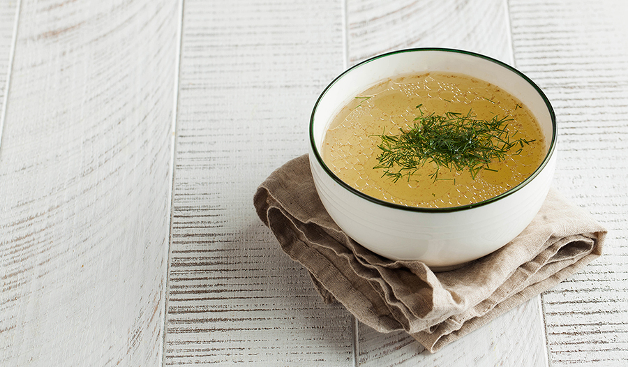 Homemade bone broth in a white bowl on a white wooden background