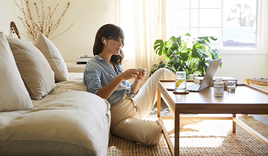 Woman working at home in living room drinking coffee, water, and taking ashwagandha supplement