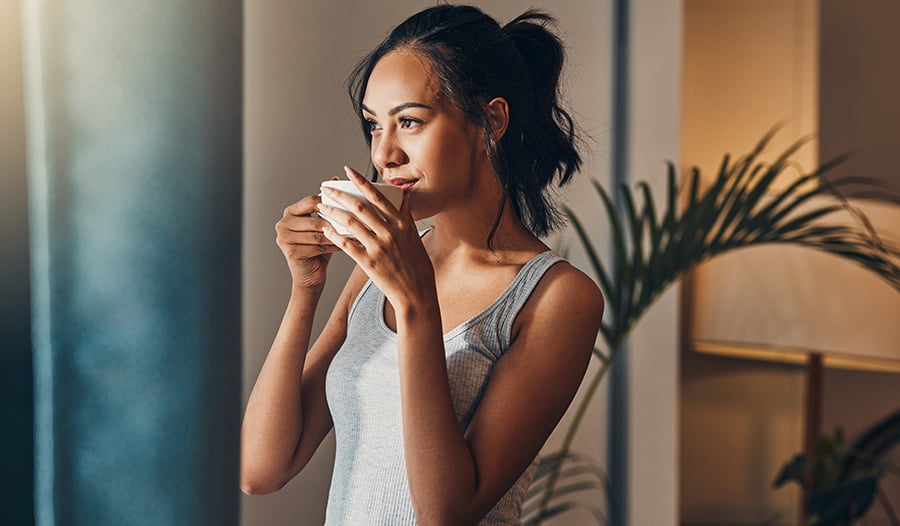 Woman drinking coffee at home looking out windown