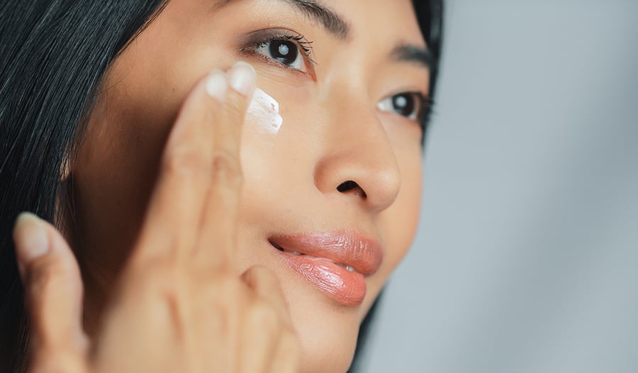 Beautiful woman applying skincare moisturizer to face