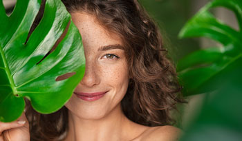 woman with monsterra plant leaf in front of one eye