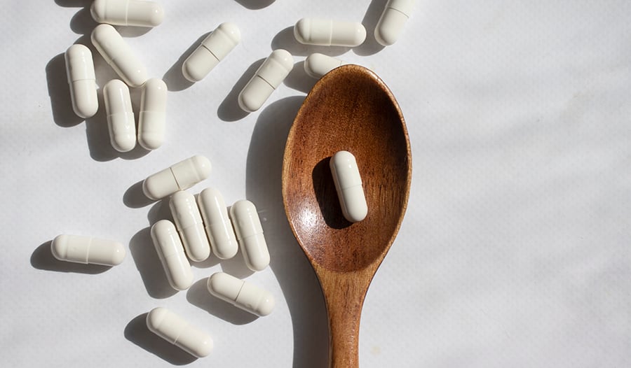 Wooden spoon with probiotic capsules scattered on table