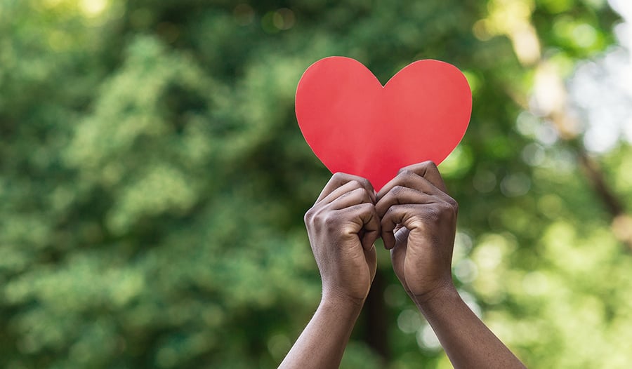 Hands holding red paper heart on green background