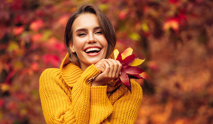 woman in yellow sweater holding autumn leaves