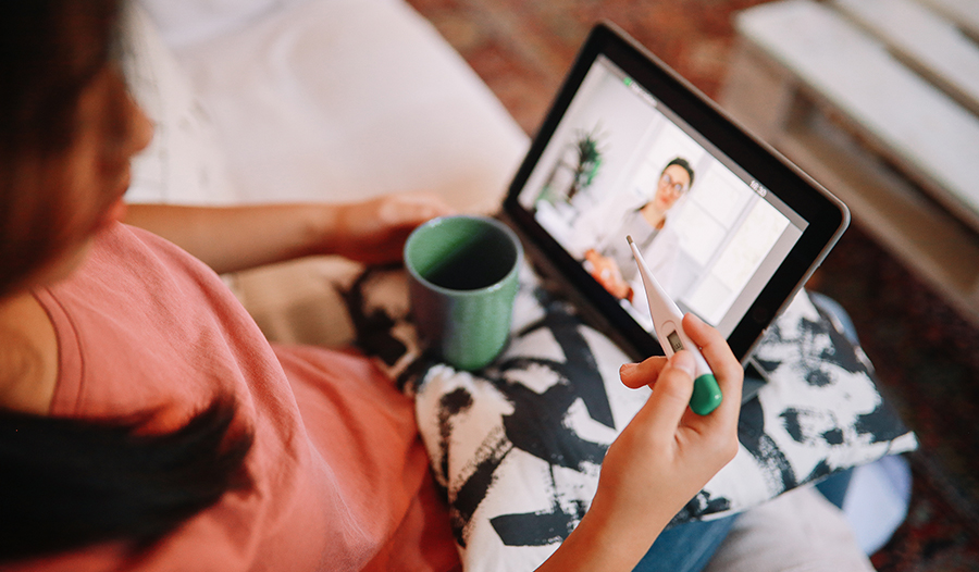 Young woman checking her temperature using an iPad or tablet to video call a doctor