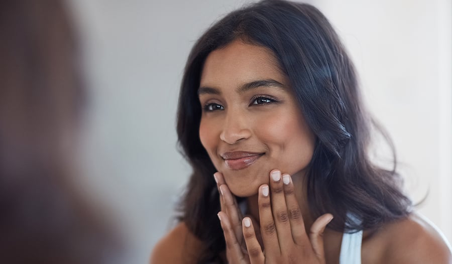 woman looking at her skin in mirror thinking of questions to ask her dermatologist