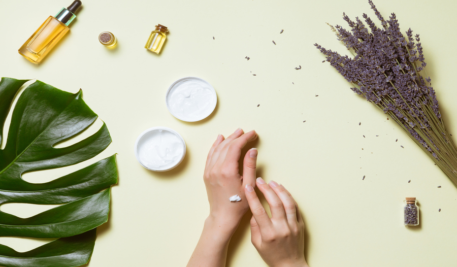 dry hands with a dab of lotion against a yellow background and a palm leaf, oils and other moisturiz