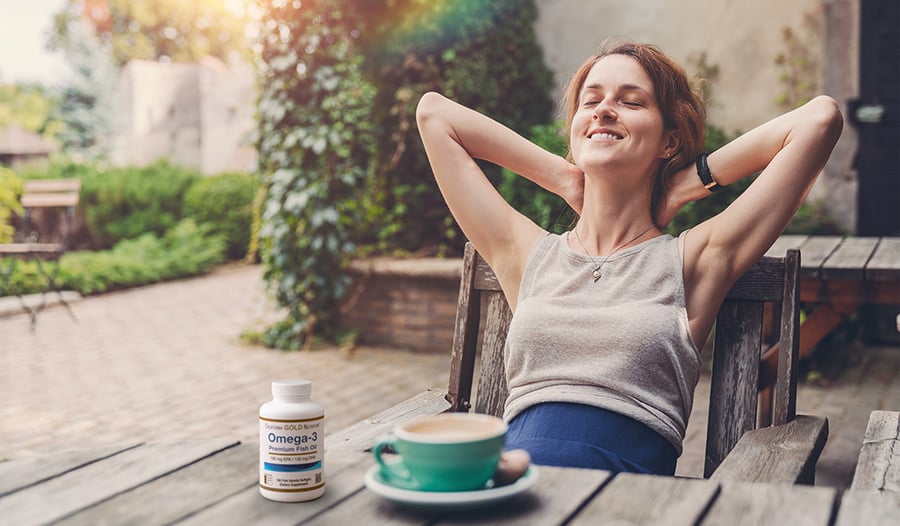 Woman relaxing outside with coffee and omega-3 supplement on table
