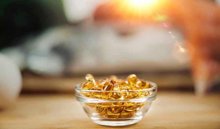 Fish oil supplements in glass bowl on table with sun in the background