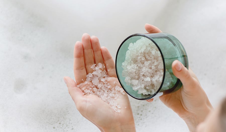 Hands pouring epsom salt into bath water