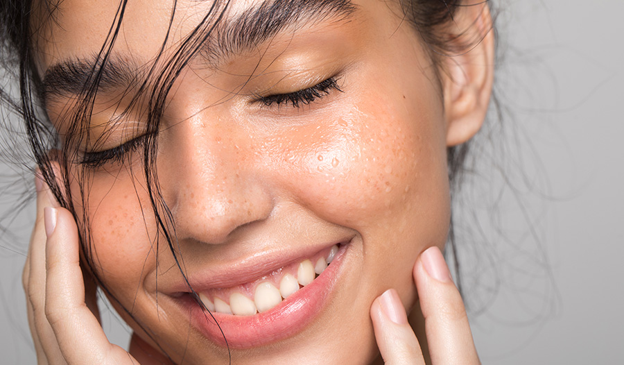 woman with exfoliating toner on her face smiling at the camera with eyes closed