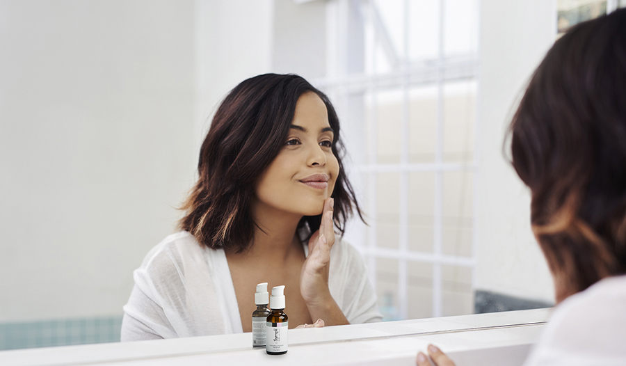 Young woman looking at her skin in bathroom mirror