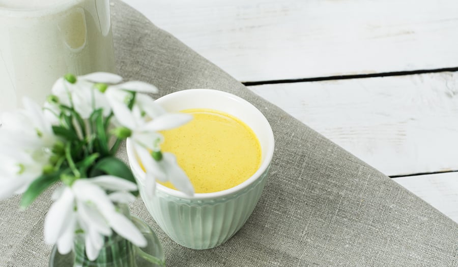 Cup of turmeric golden milk on white table with flowers
