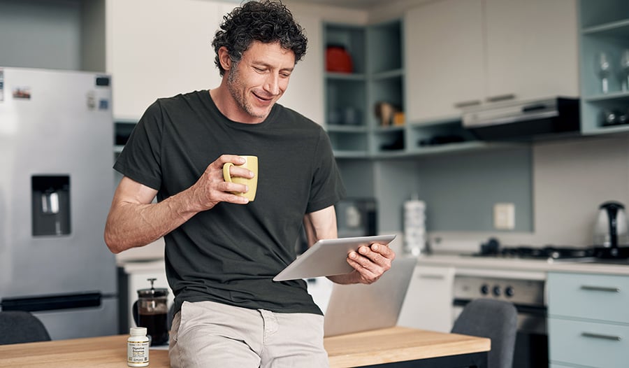 Man drinking coffee in kitchen looking at tablet