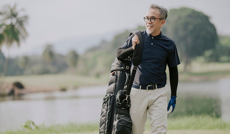 Male golfer walking on golf course carrying bag