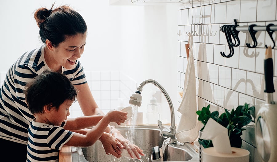 Asian boy washing dishes with his mother in the kitchen