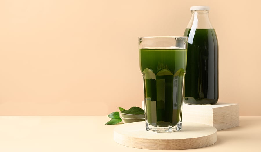 Green drink in clear glass with greens powder supplement in bowl