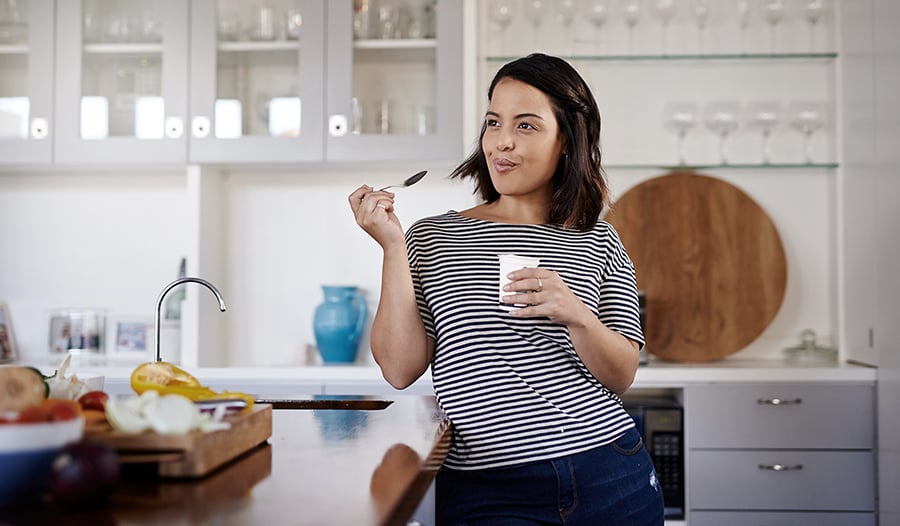 Young woman in striped shirt eating yogurt cup at home