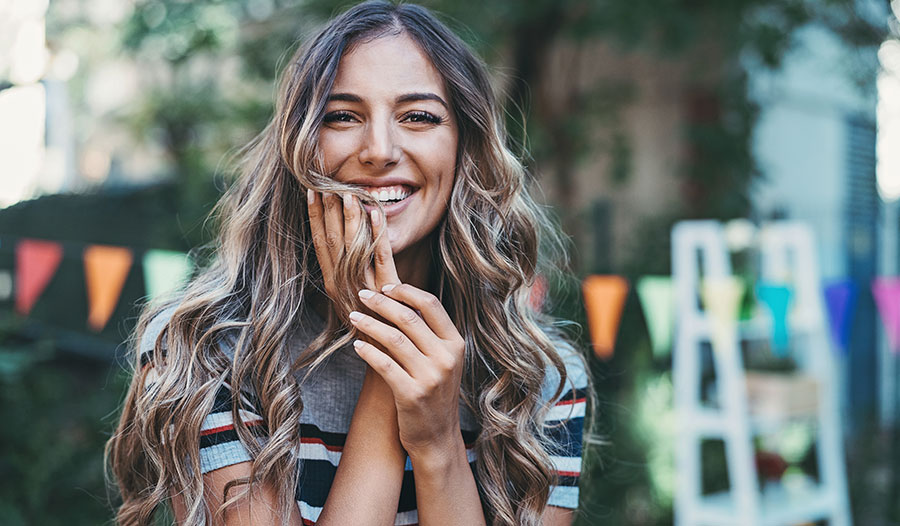 woman with long curly hair smiling while holding some of her hair