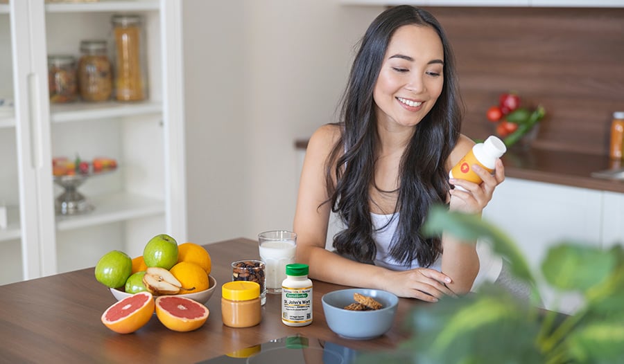 Young healthy woman at kitchen table examining supplement label